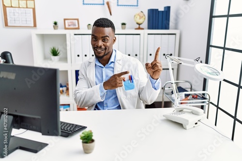 Young african doctor man wearing stethoscope at the clinic smiling and looking at the camera pointing with two hands and fingers to the side.