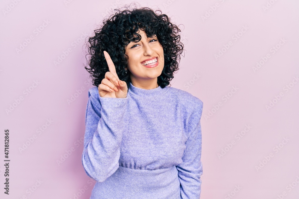 Young middle east woman wearing casual clothes showing and pointing up with finger number one while smiling confident and happy. Young middle east woman wearing casual clothes showing and pointing up with finger number one while smiling confident and happy.