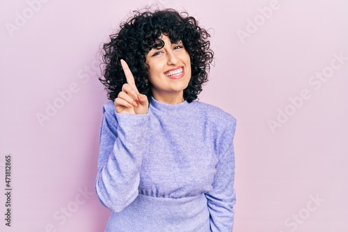 Young middle east woman wearing casual clothes showing and pointing up with finger number one while smiling confident and happy. © Krakenimages.com