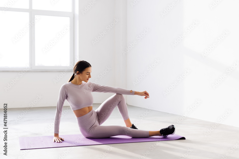 Female in sportswear sitting on yoga mat and smiling after workout. Young woman taking a break from workout session at gym.