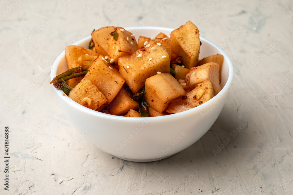 Korean marinated daikon radish in a white bowl on a light background. Korean marinated daikon radish in a white bowl on a light background.