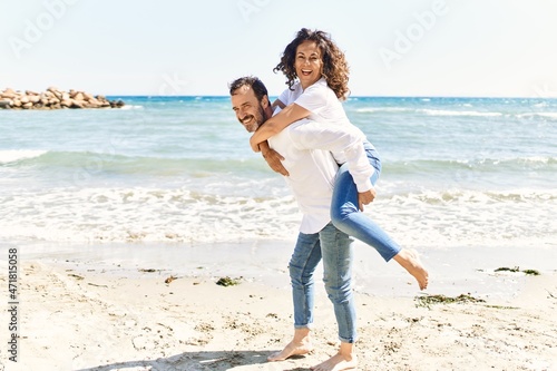 Middle age hispanic man smiling happy holding woman on his back at the beach.