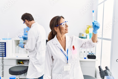 Middle age man and woman partners wearing scientist uniform holding test tube at laboratory