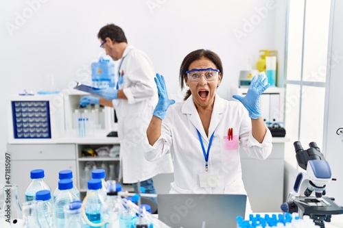 Middle age woman working at scientist laboratory celebrating victory with happy smile and winner expression with raised hands