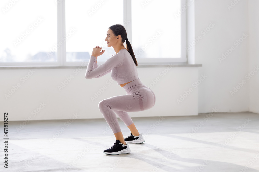 Young beautiful woman squats at gym windows Young beautiful woman squats at gym windows