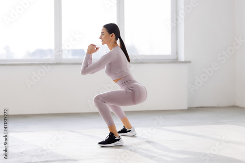 Young beautiful woman squats at gym windows