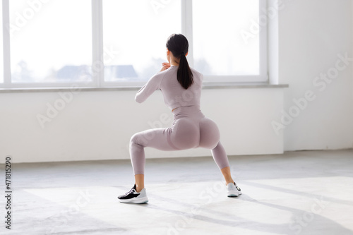 Young beautiful woman squats at gym windows