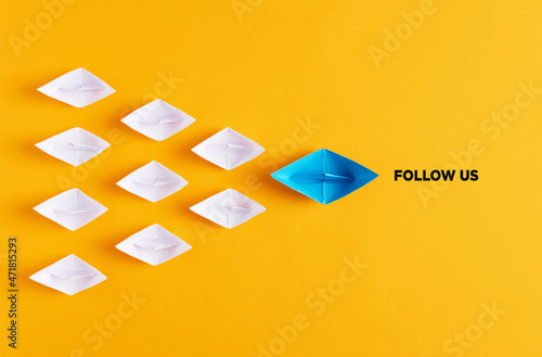 Yellow paper boat leads white paper ships with the follow us message. Social media or internet followers concept.