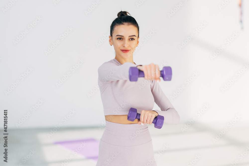 Attractive young fitness woman holding dumbells at gym hall Attractive young fitness woman holding dumbells at gym hall