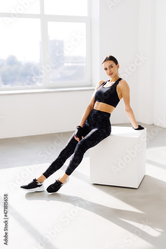 Young woman sitting on a box at gym after her workout. Female athlete taking rest after exercising at gym.