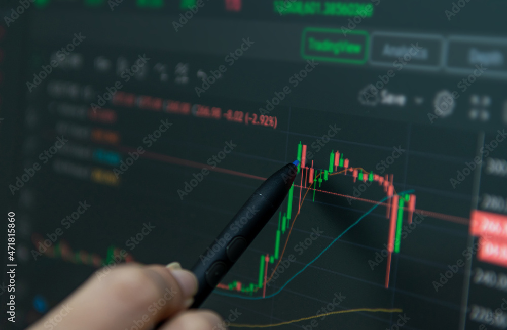 Hand holding a pen to analyze financial graphs on a computer monitor. Hand holding a pen to analyze financial graphs on a computer monitor.