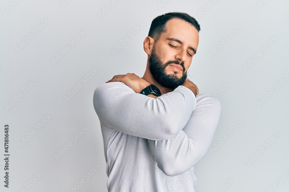 Young man with beard wearing casual white shirt hugging oneself happy and positive, smiling confident. self love and self care Young man with beard wearing casual white shirt hugging oneself happy and positive, smiling confident. self love and self care