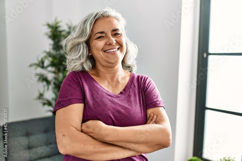 Middle age grey-haired woman smiling happy standing with arms crossed gesture at home.