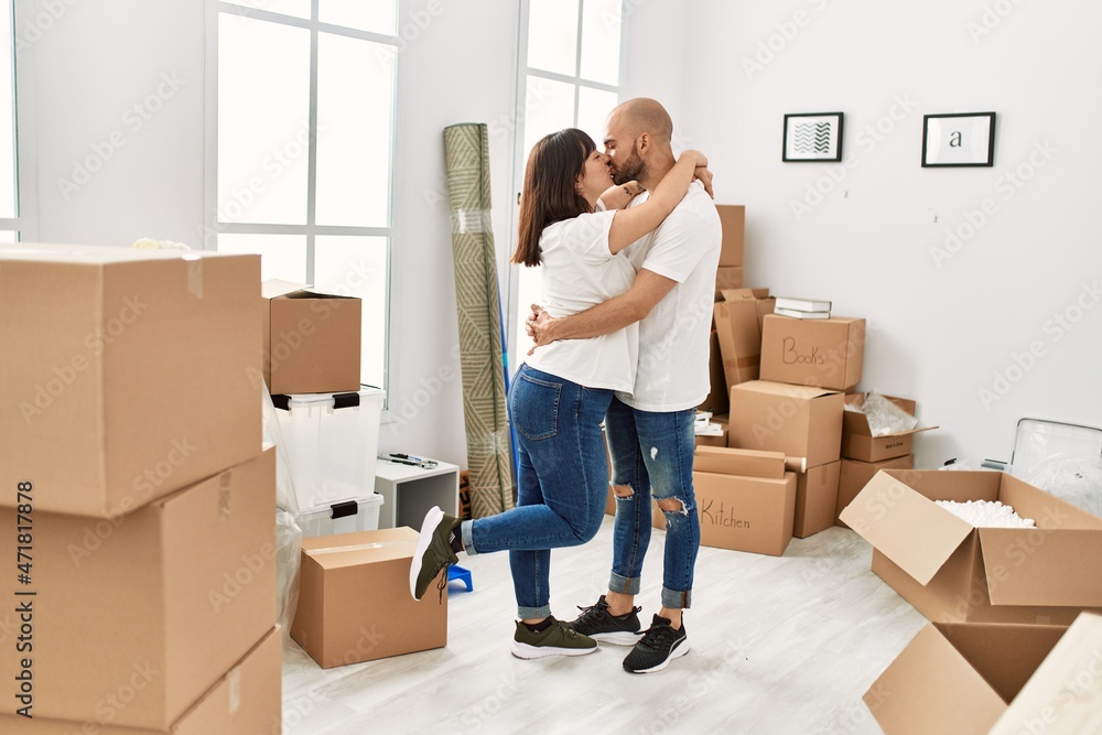 Young hispanic couple kissing and hugging moving at new home. Young hispanic couple kissing and hugging moving at new home.