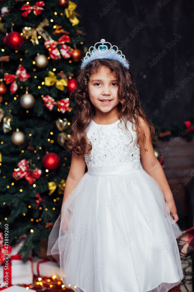 beautiful little girl in a white dress like a princess at a Christmas tree beautiful little girl in a white dress like a princess at a Christmas tree