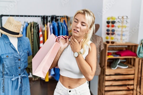 Young caucasian woman holding shopping bags at retail shop touching painful neck, sore throat for flu, clod and infection