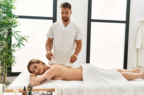 Young caucasian woman at physiotherapy clinic getting muscle massage by professional therapist. Physiotherapist man doing tea bag treatment to client