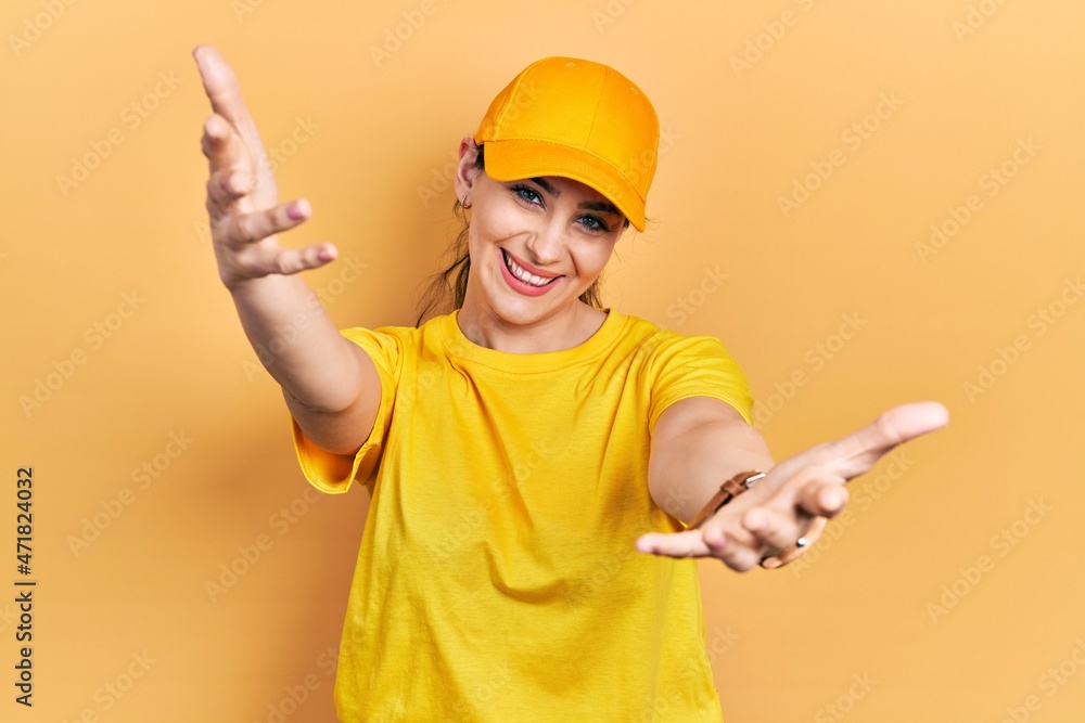 Young hispanic woman wearing delivery uniform and cap looking at the camera smiling with open arms for hug. cheerful expression embracing happiness. Young hispanic woman wearing delivery uniform and cap looking at the camera smiling with open arms for hug. cheerful expression embracing happiness.
