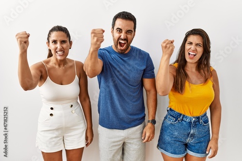 Group of young hispanic people standing over isolated background angry and mad raising fist frustrated and furious while shouting with anger. rage and aggressive concept.