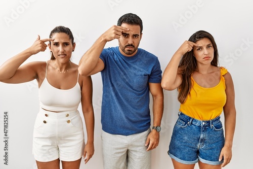 Group of young hispanic people standing over isolated background pointing unhappy to pimple on forehead  ugly infection of blackhead. acne and skin problem