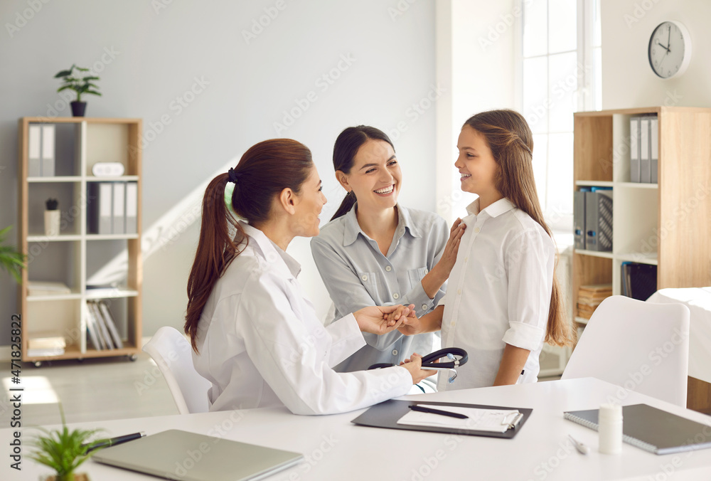 Children's medical care. Happy mother and daughter at medical examination at friendly female pediatrician. Smiling doctor and mother encourage teenage girl during medical consultation at hospital. Children's medical care. Happy mother and daughter at medical examination at friendly female pediatrician. Smiling doctor and mother encourage teenage girl during medical consultation at hospital.