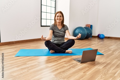 Middle age caucasian woman smiling confident having online yoga class at sport center