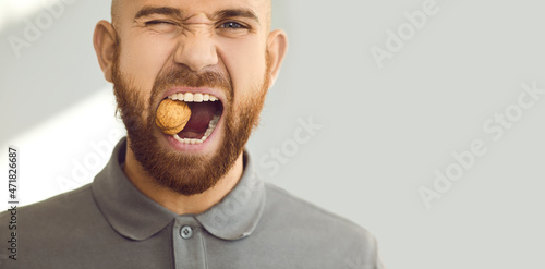 Confident, charismatic, handsome man winks his eye and cracks a hard nut. Close up head shot of a young ginger guy demonstrating his healthy teeth and trying to crack a walnut. Dental health concept photo