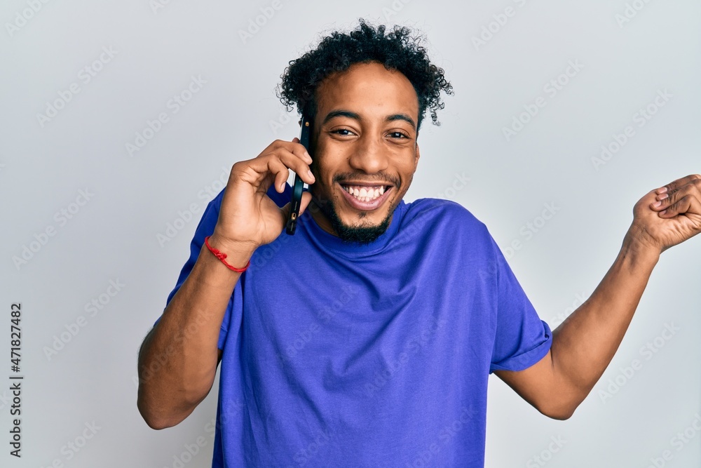 Young african american man with beard having conversation talking on the smartphone screaming proud, celebrating victory and success very excited with raised arm Young african american man with beard having conversation talking on the smartphone screaming proud, celebrating victory and success very excited with raised arm