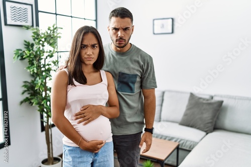 Young interracial couple expecting a baby, touching pregnant belly skeptic and nervous, frowning upset because of problem. negative person.