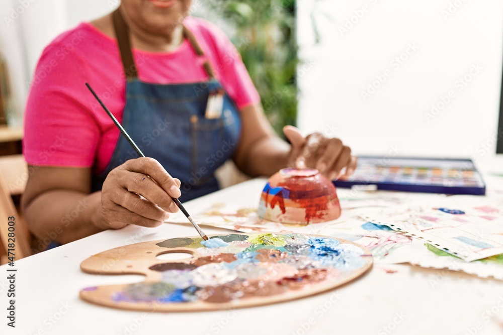Naklejka premium Senior african american woman painting clay ceramic at art studio