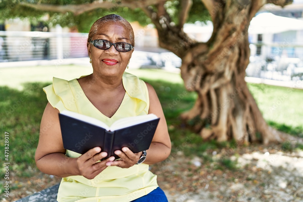 Fototapeta premium Senior african american woman reading book sitting on the bench at the park.