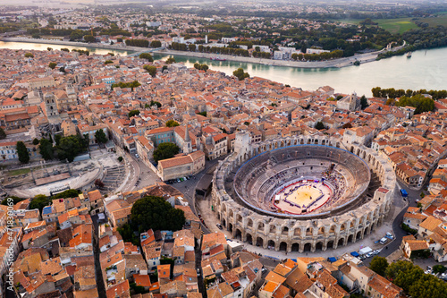 Aerial view of Arles townscape on bank of Rhone river overlooking restored antique Roman amphitheatre and ruins of Gallo-Roman theatre on autumn day, France