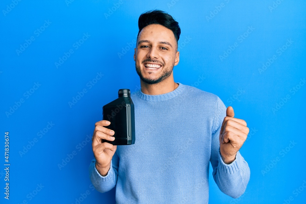 Young arab man holding motor oil bottle screaming proud, celebrating victory and success very excited with raised arm Young arab man holding motor oil bottle screaming proud, celebrating victory and success very excited with raised arm