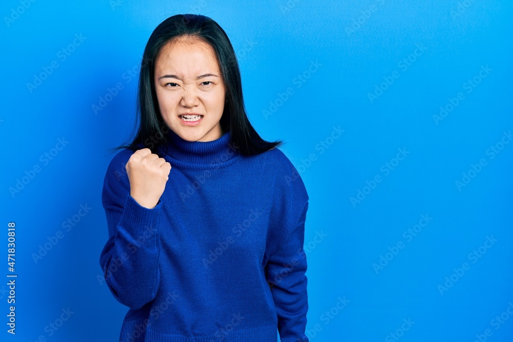 Young chinese girl wearing casual clothes angry and mad raising fist frustrated and furious while shouting with anger. rage and aggressive concept. Young chinese girl wearing casual clothes angry and mad raising fist frustrated and furious while shouting with anger. rage and aggressive concept.