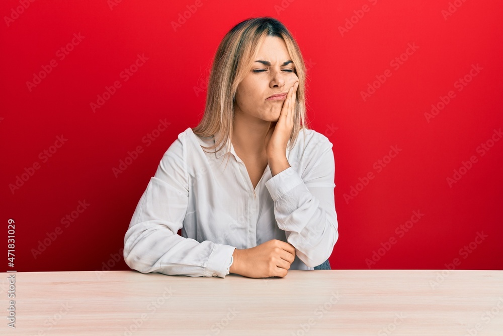 Young caucasian woman wearing casual clothes sitting on the table touching mouth with hand with painful expression because of toothache or dental illness on teeth. dentist Young caucasian woman wearing casual clothes sitting on the table touching mouth with hand with painful expression because of toothache or dental illness on teeth. dentist