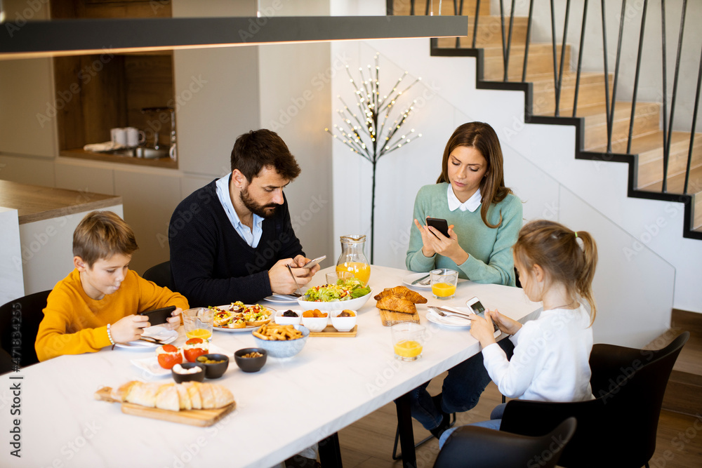 © BGStock72 - Family using mobile phones while having breakfast at dining table at apartment