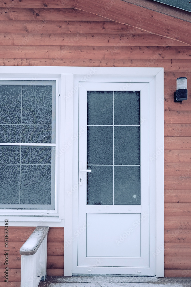 Fototapeta premium Window panes and the front door covered in hoarfrost. Plastic entrance panel, door and window.