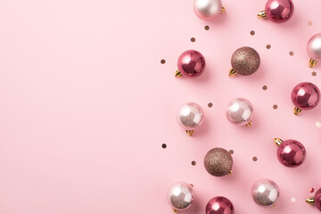 Top view photo of pink christmas tree decorations balls and shiny confetti on isolated pastel pink background with blank space