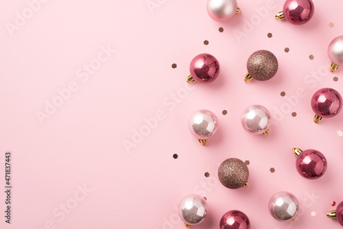 Top view photo of pink christmas tree decorations balls and shiny confetti on isolated pastel pink background with blank space