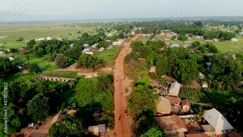 Motorcycle traffic along a red dirt unpaved road in rural Rukubi, Nigeria - aerial flyover photo