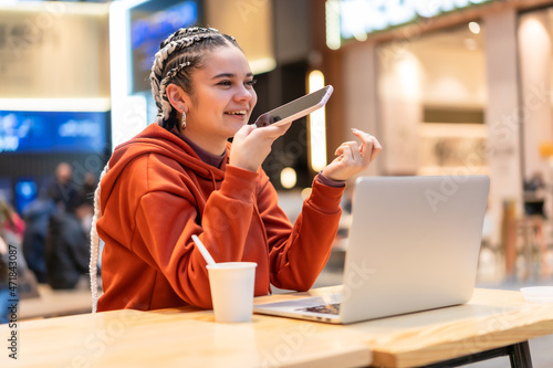 Alternative girl with white braids using a computer in a shopping mall, smiling making an audio message