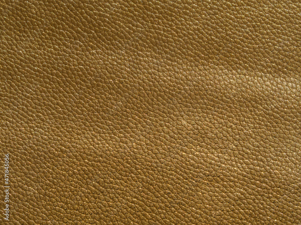 The texture of artificial leather is golden in color. Yellow textured background with reflections of light. Close-up of the skin The texture of artificial leather is golden in color. Yellow textured background with reflections of light. Close-up of the skin