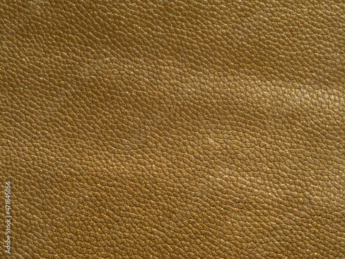 The texture of artificial leather is golden in color. Yellow textured background with reflections of light. Close-up of the skin