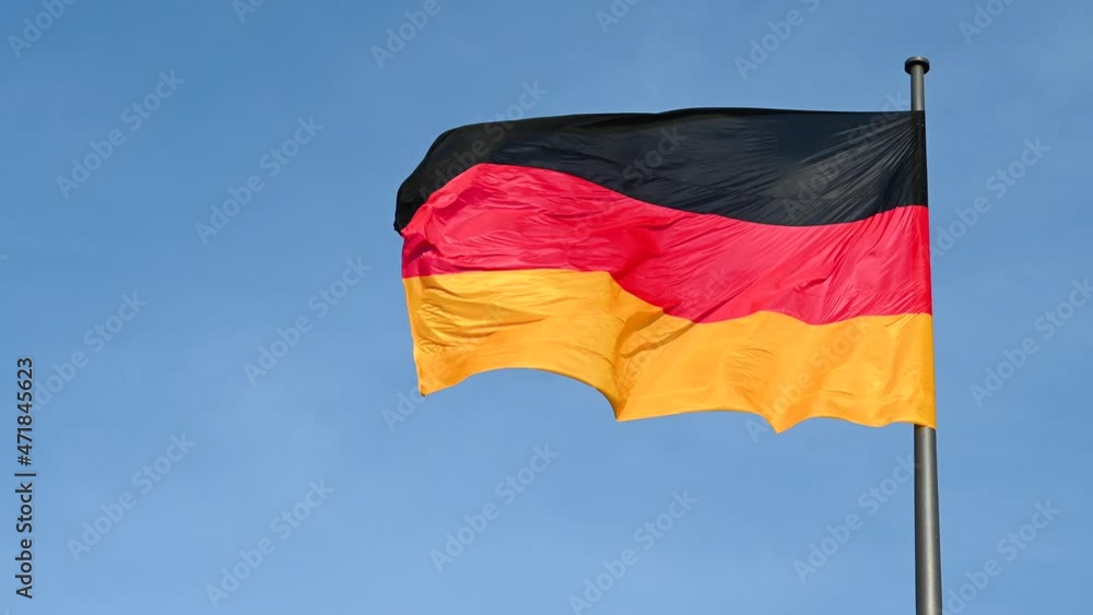 Slow motion of German flag flying on the wind. Waving flag on flagpole against blue sky in Germany. Black, red and yellow colors on German flag in a front of Bundestag. Symbol of German people. 