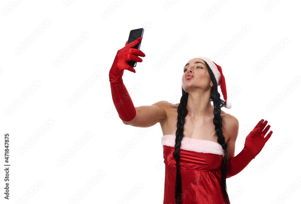 Attractive sexy dark-haired young woman with two pigtails sending kisses while taking a selfie, looking into the camera on a smartphone in her outstretched hand. Copy ad space. Christmas concept Attractive sexy dark-haired young woman with two pigtails sending kisses while taking a selfie, looking into the camera on a smartphone in her outstretched hand. Copy ad space. Christmas concept
