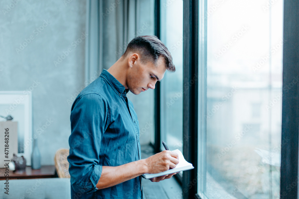 man making notes in a notebook, standing near the window. man making notes in a notebook, standing near the window.