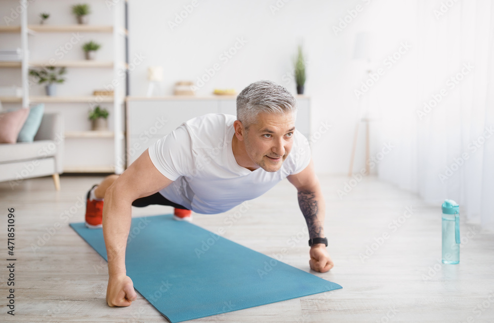 Fototapeta premium Strong senior man making strength workout, doing push ups on sports mat, exercising at home, copy space