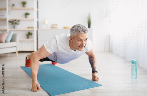 Strong senior man making strength workout, doing push ups on sports mat, exercising at home, copy space