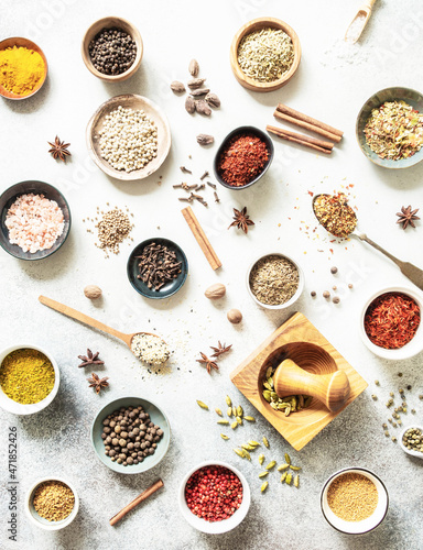 Various dry spices in small bowls and spoons flat lay on grey background.
