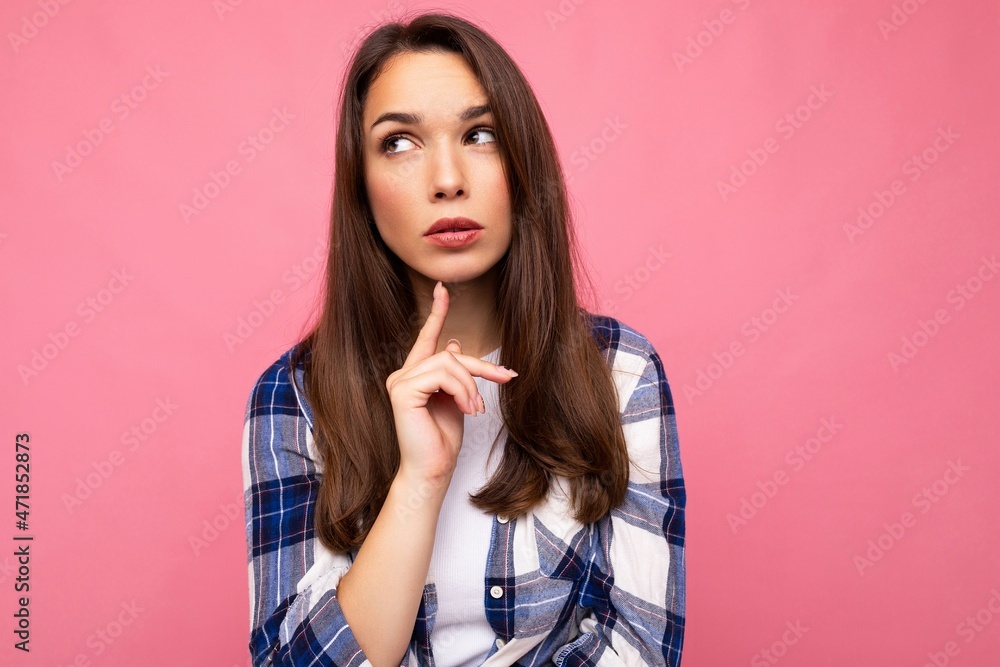 Photo portrait of young beautiful thinking and dreaming brunette woman in trendy blue and white shirt. Female person posing isolated near pink wall with empty space in studio Photo portrait of young beautiful thinking and dreaming brunette woman in trendy blue and white shirt. Female person posing isolated near pink wall with empty space in studio